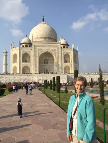 An elderly woman stands in front of the Taj Mahal.